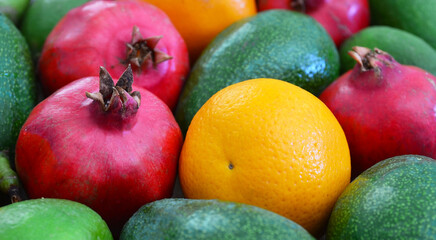 Assorted fresh ripe tropical fruits as a background.Avocado,orange,lime and pomegranate.Exotic fruits,vegan food or diet concept.Selective focus.