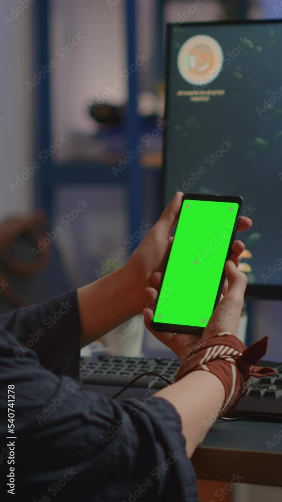 Poster vertical video: professional cyber gamer looking at phone with greenscreen, chroma key, mock up desk
