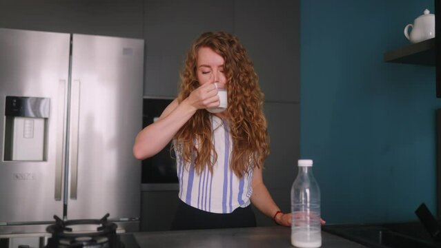 Woman drinks expired milk and suffering from severe stomach ache standing on kitchen. Female with lactose intolerance tries poor quality cow milk. Girl with digestive problems feels bad pain in belly.