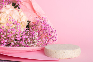 A minimalistic scene of a lying stone with a bouquet of hydrangea flowers on a light pink background.