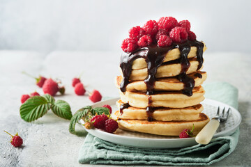 American pancakes. Stack pancakes with fresh raspberry with chocolate glaze or toppings in white bowl on light gray table background. Homemade classic american pancakes. Magazine concept. Top view.