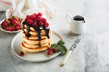American pancakes. Stack pancakes with fresh raspberry with chocolate glaze or toppings in white bowl on light gray table background. Homemade classic american pancakes. Magazine concept. Top view.