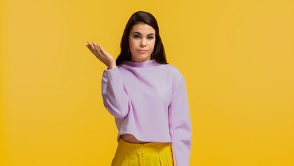 displeased young woman in purple sweatshirt standing and looking at camera isolated on yellow