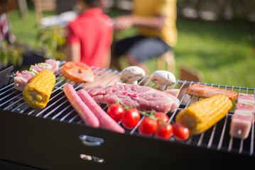 Steak, sausages and fresh vegetables on BBQ. Juicy raw meat, mushrooms and yellow corn grilling. BBQ, cooking, food concept