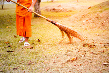 The monk sweeps leaves to collect trash in the temple courtyard.