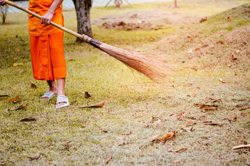 Naklejka premium The monk sweeps leaves to collect trash in the temple courtyard.