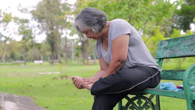 Asian elderly woman hurts her ankle After a walk in the park. Sports concept. Senior exercise injuries