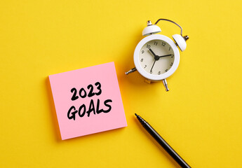 2023 goals message on pink note paper with alarm clock and pen. Planning personal or business goals...