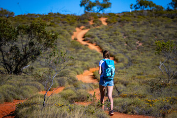 fit girl with backpack hiking uphill on red rocks in cape range national park in western australia,...