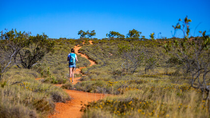 Naklejka premium fit girl with backpack hiking uphill on red rocks in cape range national park in western australia, hiking in australian outback, australian desert