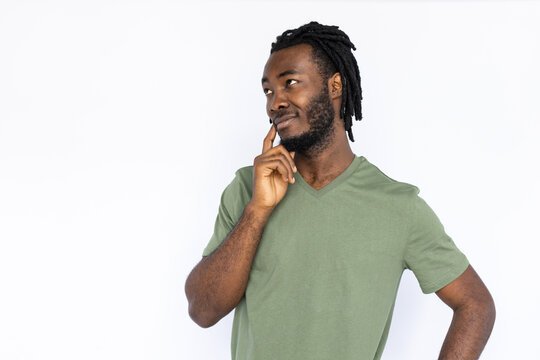 Portrait of charming African American man touching cheek. Pleased young male model with braided dark hair in green T-shirt smiling, looking away at ads. Advertisement concept.