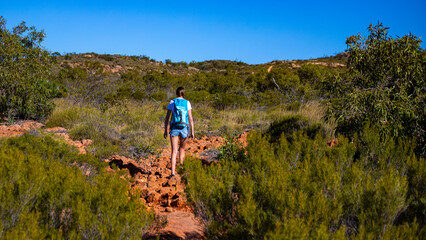 fit girl with backpack hiking uphill on red rocks in cape range national park in western australia,...