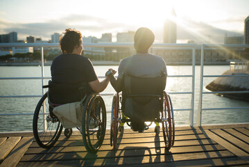 Relaxed biracial family having romantic date. African American man and Caucasian woman in wheelchairs, holding hands, looking at sunset. Love, affection, happiness concept