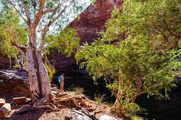girl in shorts hiking in karijini national park, western australia; hiking on the edge of a gorge in the australian outback; red soil and red rocks