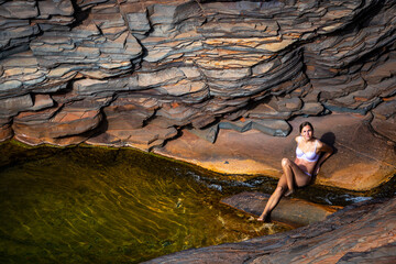 a long-haired girl in a white bikini takes a refreshing dip in a rock pool in karijini national park in western australia, an oasis in the middle of the desert in the australian outback