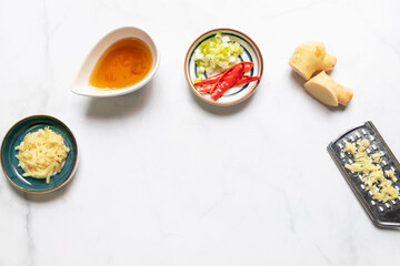Ingredient for delicious steam with soy sauce. Soy sauce, ginger grate with a handheld grater, scallion and chili. Top view on white table background with copy space.