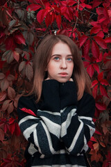 Autumn portrait of a beautiful cute woman against a background of bright red leaves. Warm black sweater