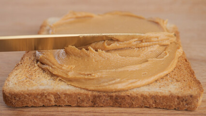 Peanut butter. Peanut Butter Spreading on bread with a golden knife, close up. Perfect breakfast
