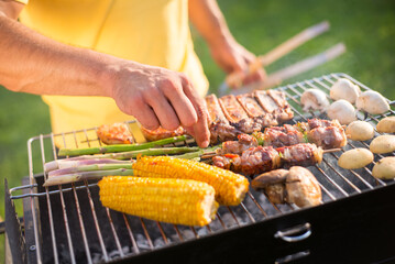 Close-up of man grilling tasty meat and vegetables. Man in yellow T-shirt standing near BBQ grid. BBQ, cooking, food concept