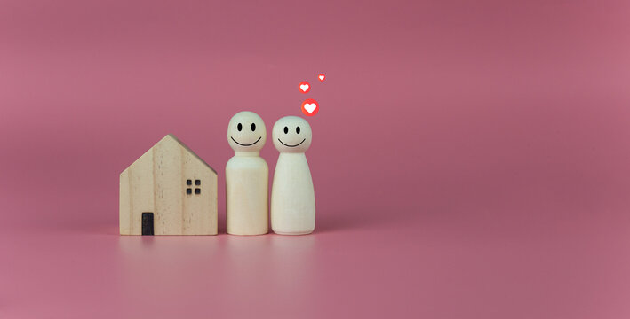 Happy house concept. Model house with wooden dolls standing lined up on pink background and heart icons. Indicates happiness and love in the home.
