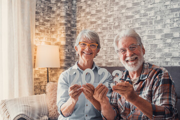 Portrait of couple of two old pensioners holding together numbers of 2023 at home. Close up of new...