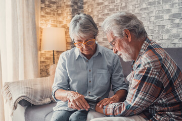 Close up and portrait of old woman checking pressure of his husband at home sitting not he sofa....