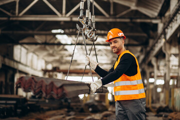 Man working at steel factory with a crane lifting steel pipes