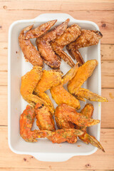 Flat lay view of a tray of assorted chicken wings on a wood table.