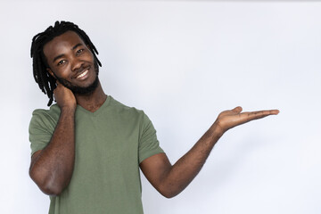 Portrait of cheerful African American man pointing palm at ads. Happy young male model with braided dark hair in green T-shirt smiling, touching neck and looking at ads. Advertisement concept.