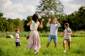Fototapeta premium Parents with children playing ball in the park on green grass