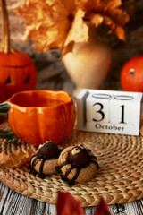 Traditional aesthetic autumn Halloween cookies in shape of spider and cup of tea in shape of pumpkin. 31 of October on calendar.