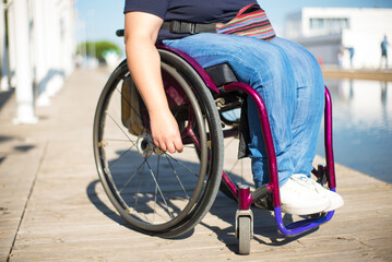 Close-up of colorful wheelchair. Caucasian female hand on wheel of wheelchair during walk in park. Disability concept