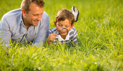 Naklejka na ściany i meble Father and son watching bugs in the grass using magnifying glass