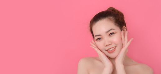 Obraz na płótnie Canvas Close up photo of cute Asian woman raising her hand showing her healthy skin on a pink background. Beauty and skin care concept.