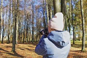 Photographer woman with DSLR camera and zoom lens take pictures of bare trees in European autumn Park
