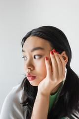 Fototapeta na wymiar Portrait of young asian woman with red manicure touching face isolated on grey