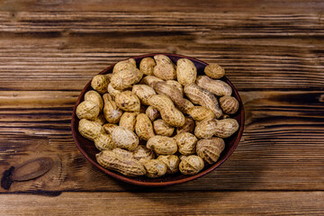 Ceramic plate with heap of unpeeled peanuts on wooden table