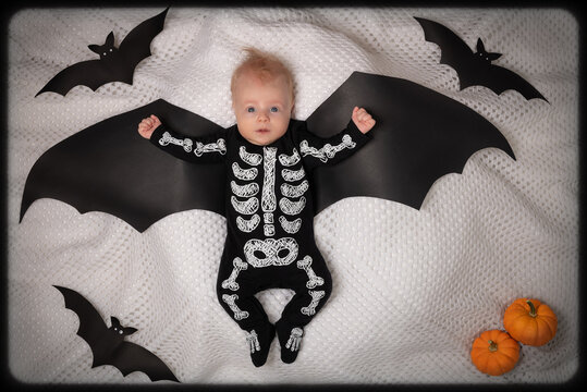Happy Halloween. Little baby boy dressed funny skeleton with wings, orange pumpkins and black bats. Child wearing Haloween costume. Top view.