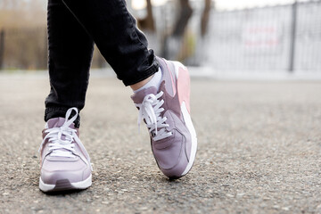 Plakat cropped image of female legs in shoes. Woman in black jeans and pink sneakers stands on pavement