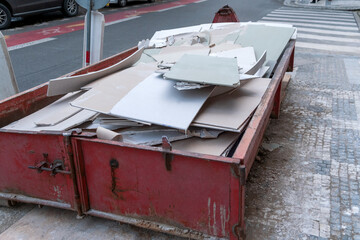 Heap of used drywall loaded in dumpster waste, metal red container filled with construction waste, near a construction site. - obrazy, fototapety, plakaty