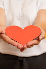 vertical image of a paper heart stretched out on the palms of a woman