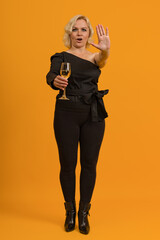 Fototapeta na wymiar blonde woman holding a glass of champagne and showing a stop sign with her hand on a colored background