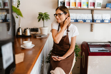 Mature barista woman using mobile phone while working at cafe