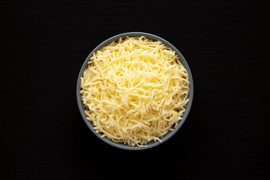 Shredded Mozzarella Cheese In A Bowl On A Black Surface, Top View. Flat Lay, Overhead, From Above.