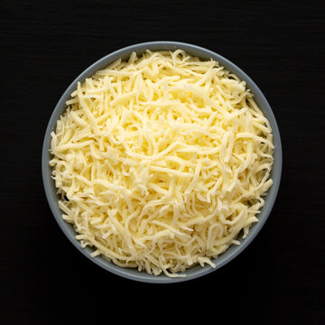 Shredded Mozzarella Cheese in a Bowl on a black surface, top view. Flat lay, overhead, from above.
