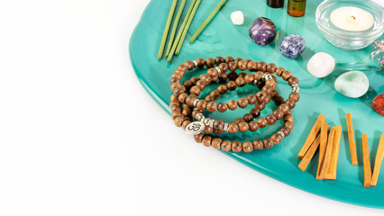 Naklejka premium Self-care, healing composition with rosary beads, aroma sticks, chakra stones, sandalwood sticks and candle on a green marble podium with copy space. Concept of relax, energy healing and meditation