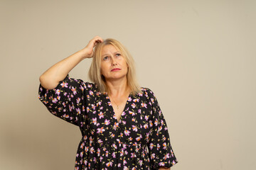 Hmm, you must think. The blonde-haired girl pondered, scratching her head in doubt and uncertainty, her face puzzled and indecisive. Shot in a separate indoor studio on a beige background.