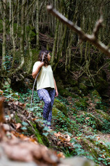 young hiker standing in the forest. woman posing among the trees on an autumn afternoon. she holds a large branch for support while looking at the landscape around her.
