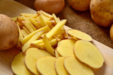 piece of slicing and cutting on wooden desk and tubers of raw potatoes on burlap close up. Selective focus