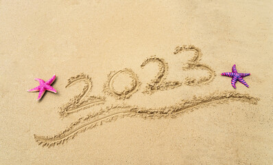 Fototapeta na wymiar 2023 handwritten with starfish in sand on a beautiful beach